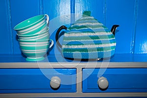 Teapot with blue and green knitted tea cosy and cups