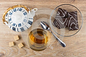 Teapot, chocolate swiss rolls, cup with tea, lumpy sugar, teaspoon