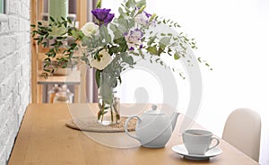 Teapot, cup and flowers on wooden dining table. Kitchen interior
