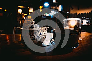 A teapot, a cup and a tealight inside a glass over a wooden table of a cozy Irish pub