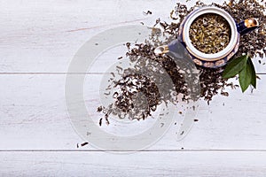 Teapot and dried tea leaves on white wooden background, green tea leaf on table, black herbal homemade hot beverage in porcelain