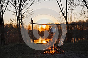 Teapot on the fire prepares tea. Orange sunset