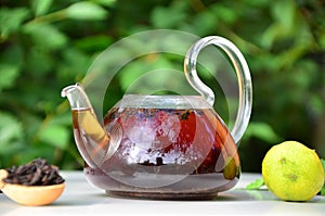 teapot full of tea on a background of green foliage on a wooden table, next to forest berries, raspberries and