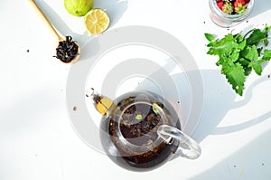 teapot full of tea on a background of green foliage on a wooden table, next to forest berries, raspberries and