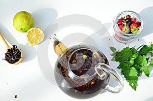 teapot full of tea on a background of green foliage on a wooden table, next to forest berries, raspberries and