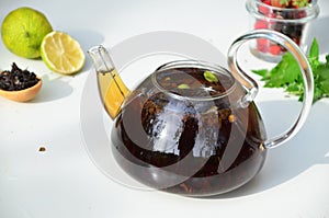 teapot full of tea on a background of green foliage on a wooden table, next to forest berries, raspberries and