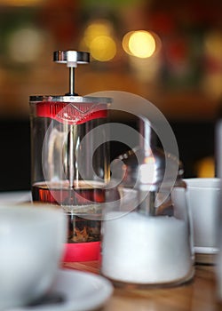 A teapot of green tea, a sugar bowl, cups are all in the foreground. On the back there is a mysterious bokeh. A cozy cafe, pleasan