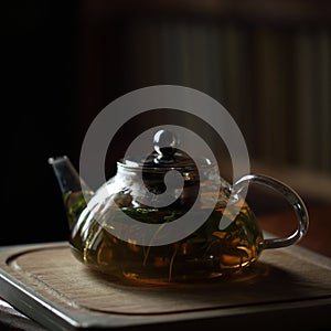 Teapot with herb tea on wooden cutting board with rosemary near, books on background, home cozy interior