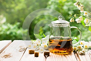 Teapot with jasmine tea and flowers on the wood background