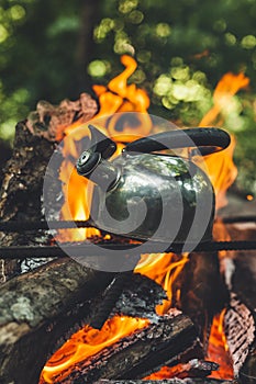 Teapot over the fire. Beautiful campfire in a tourist camp in the wild. Survival in the forest