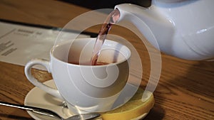 Teapot pouring fruit tea into cup close up. White cup on table in cafeteria 4k