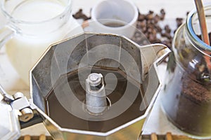 Teapot with some black coffee on a wooden table next to coffee beans, milk and a cup