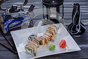 Teapot and sushi set with eel fish, nigiri, maguro and sushi rolls served on white plate on dark wooden background. Close up view.