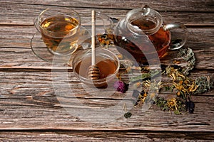 Teapot, tea in a glass Cup, sweet Golden honey and a scattering of dried herbs on a wooden background close-up.