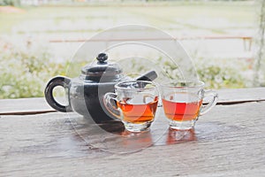 A teapot and two tea cups on a wooden floor with a rice field view