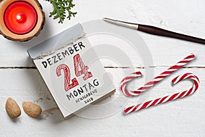 Tear-off calendar with 24th of december in German on top on a wooden surface