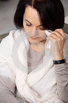 tearful mature woman holds tissue to eye