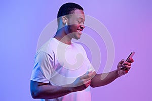 Tech Gadgets. Happy Black Guy Using Smartphone And Earpods For Listening Music
