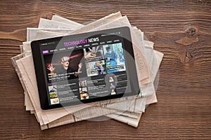 Tech news website on tablet on stack of newspapers.