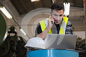 Technical engineer wearing safety vest standing in the factory workplace. Worker using smartphone and laptop talk with manager.