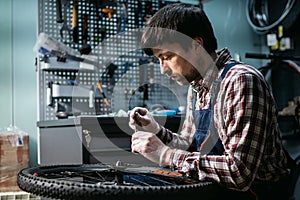 Technical expertise taking care bicycle shop. Handsome young mechanic fixing cycle wheel in workshop. Handsome repairman in