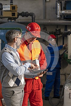 Technical Manager With Digital Tablet Standing Next to Young Worker in Industrial Interior