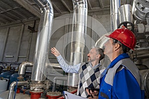 Technical Manager Standing Next to Worker and Pointing to Large Piping in Oil Refinery