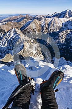 Technical mountain boots with crampons on the climber`s legs and two ice axes with a beautiful mountain landscape in the