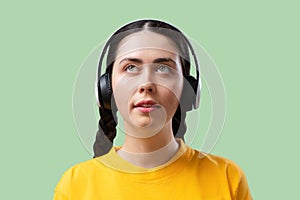 Technical support and hotline. Portrait of a young Caucasian pretty woman with headphones listening to music on a green