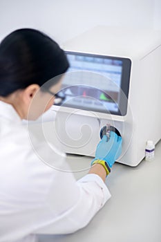 Technician in blue gloves pressing the start button of hematological analyzer