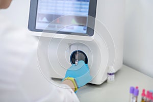 Technician in blue gloves pressing the start button of hematological analyzer in laboratory