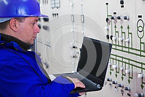 Technician in blue with laptop reading instruments in power plan