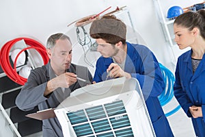 Technician checking air conditioner with apprentices