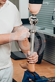 Technician checking artificial limb while at desk in workshop, adjusting it and checking for quality