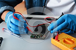 Technician checking broken smartphone at table in repair shop