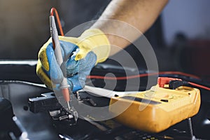 Technician checking car battery voltage with digital multimeter probe