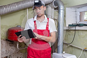 The technician checking the heating system in the boiler room with tablet in hand.