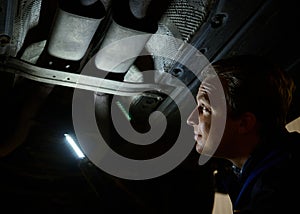 Technician checking modern car at automobile repair shop. Auto mechanic using a flashlight lamp for inspecting the bottom of the
