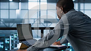 Technician coding on laptop in data center, managing server virtualization