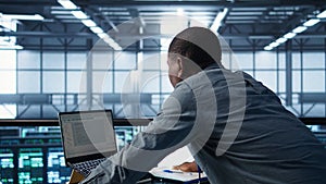 Technician coding on laptop in data center, managing server virtualization