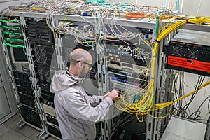 A technician connects Internet backbone wires to the server room. The specialist works near the server racks of the datacenter. A