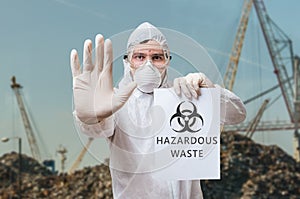 Technician in coverall warns in landfill about hazardous waste