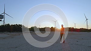 Technician engineer walking inside windmill wind turbine farm at sunset