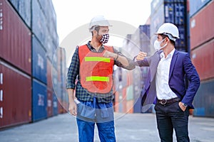 Technician or engineer workers with face mask show new style of greeting together in shipping container workplace area. Concept of