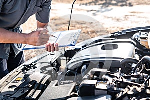 Technician engineer working of car mechanic in doing checklist for repairs engine writing to the clipboard repairing vehicle,