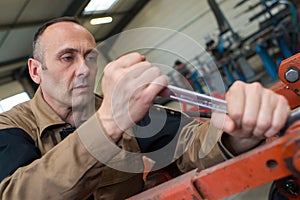 Technician in factory at machine maintenance working with wrench