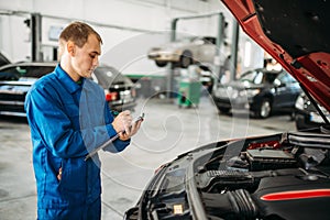 Technician fills check list, car with opened hood