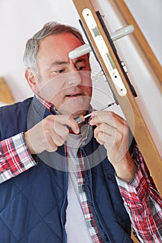 Technician fixing lock in door with screwdriver at home