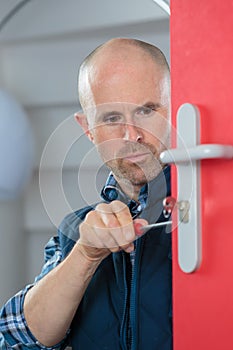 Technician fixing lock in door with screwdriver