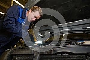 Technician, garage mechanic using flashlight luminous lamp while inspecting a car under hood in repair shop. Auto service, car